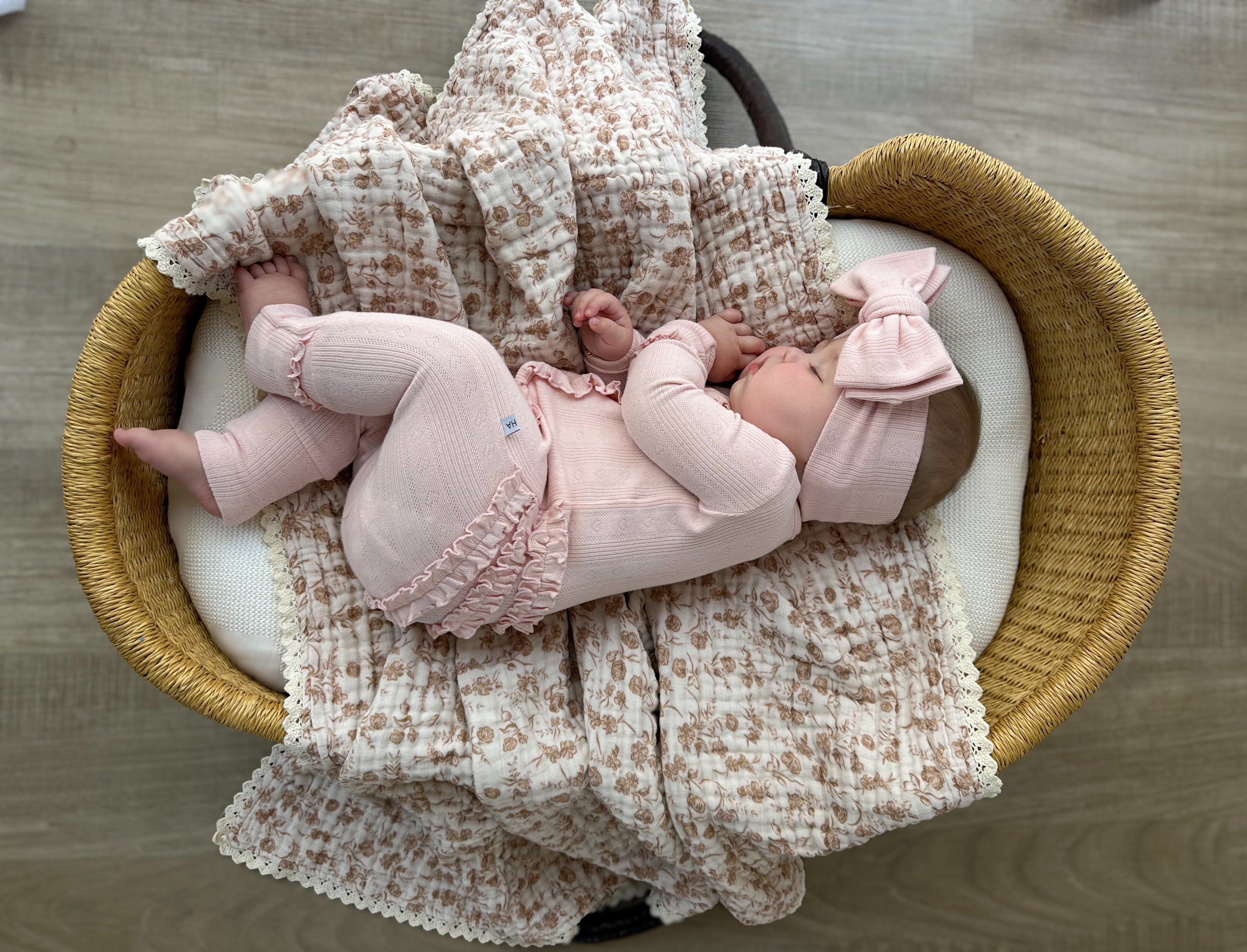 Newborn baby in pink outfit and headband lying on a textured blanket in a woven basket.